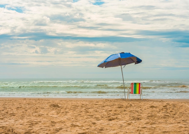 Silla de playa vacía con sombrilla azul con vistas al mar.