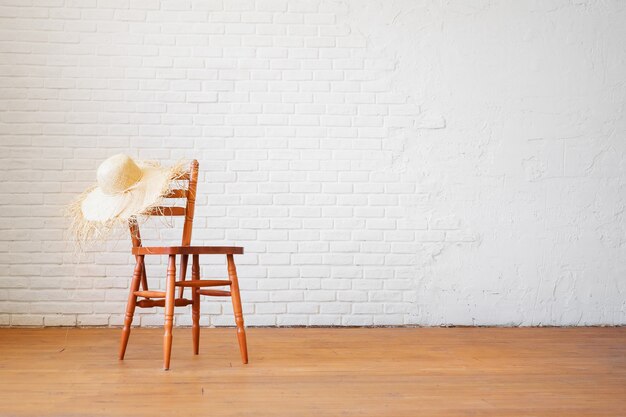 Silla retro con sombrero de paja en el fondo de una pared blanca de ladrillo vacía en el interior en estilo loft.