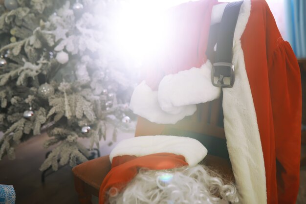 Foto silla con ropa de santa claus. traje de papá noel colgado en la sala blanca