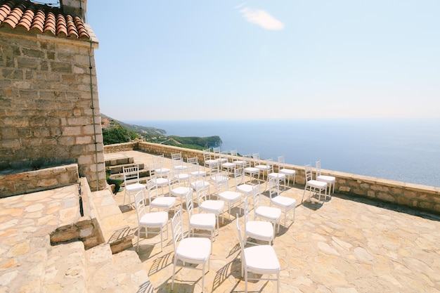 Sillas blancas para bodas cerca de la antigua iglesia con vistas a la bahía