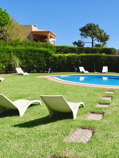 Sillas blancas en el césped cerca de la piscina en el patio trasero en Portugal Foto vertical