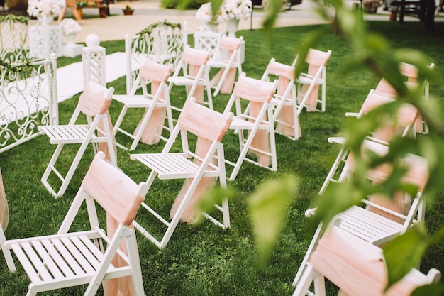 Sillas blancas decoradas con cintas rosas, se encuentran en la zona de la ceremonia nupcial en un bosque