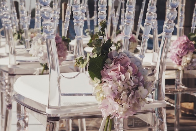 Sillas de boda blancas decoradas con flores frescas en un restaurante con vistas panorámicas al mar