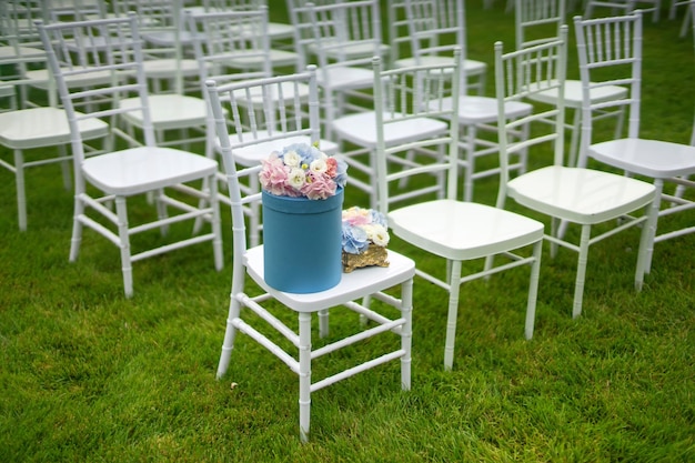 Sillas Chiavari sobre hierba En una de las sillas hay una sombrerera con flores.