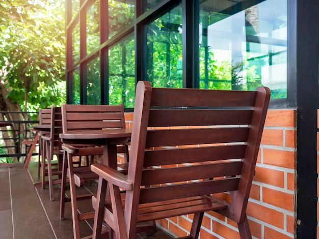 Sillas de madera acogedoras rojas vacías y mesa de centro de madera redonda cerca de la ventana de vidrio y la pared de ladrillo con jardín verde en la cafetería, en verano.