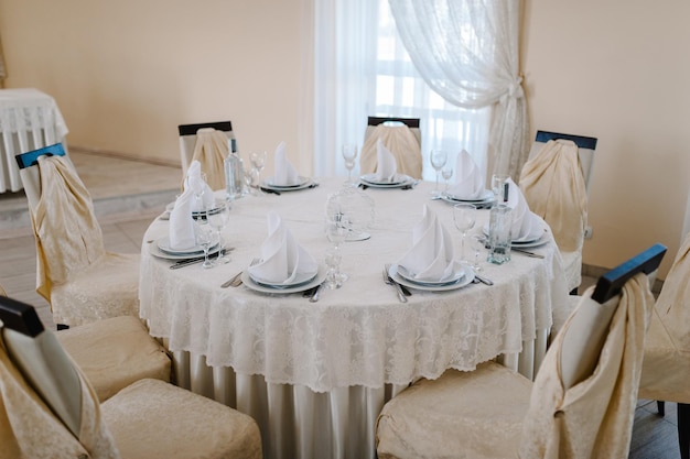 Sillas y mesas festivas decoradas y cubiertos para invitados cubiertos con un mantel servidos para estar de pie en el salón de banquetes de bodas