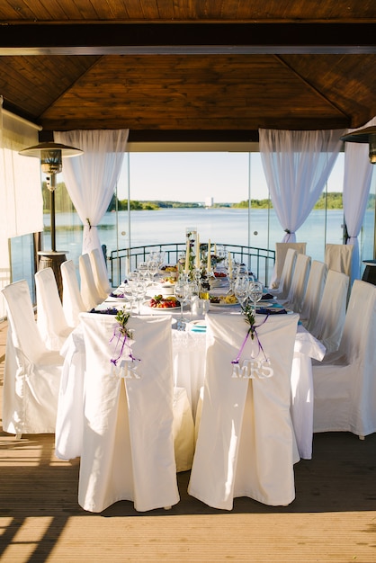 Sillas para novios con fundas blancas con las palabras "señor" y "señora" en un banquete de bodas al aire libre junto al agua