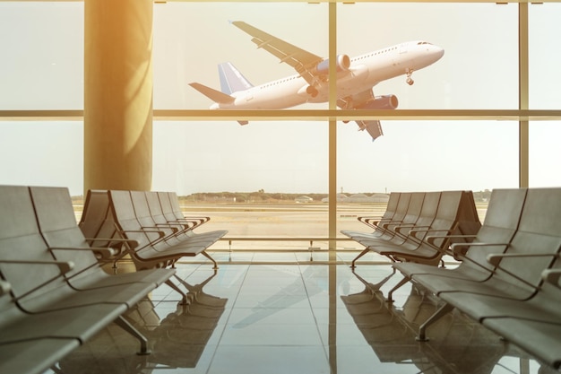 Sillas vacías en la sala de salidas del aeropuerto al fondo del avión que despega al atardecer