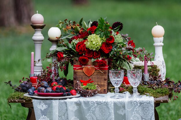 Sillas y velas, flores, platos de cerámica con frutas, de pie sobre el mantel de encaje y musgo.