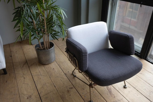 sillón decorativo gris sobre un suelo de madera con el telón de fondo de una ventana panorámica y una maceta