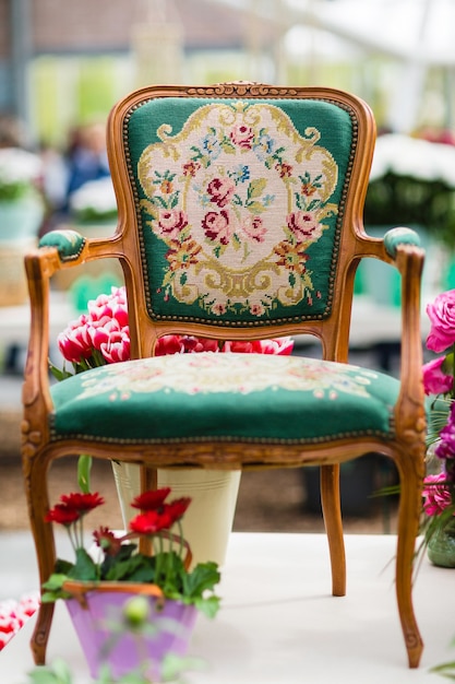 Sillón de madera con tapicería de tela y flores en segundo plano.