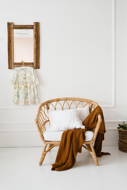 Un sillón de mimbre con una tela escocesa marrón en una habitación blanca de estilo escandinavo