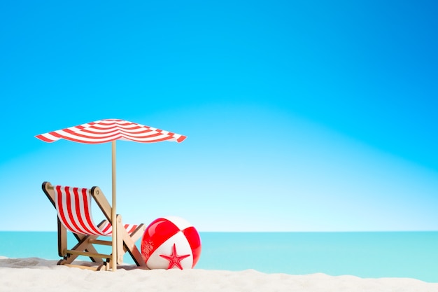 Sillón con sombrilla y pelota de playa en la costa, cielo con espacio de copia