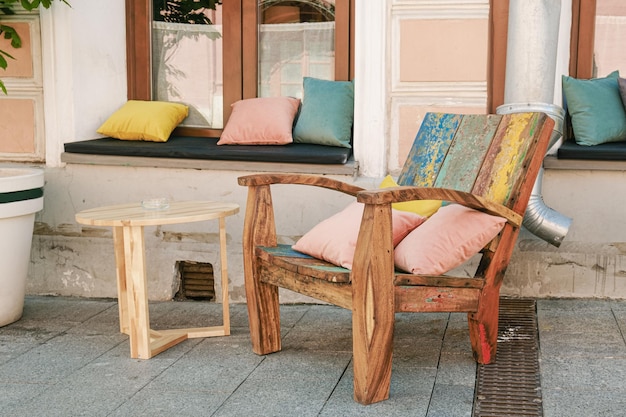 Sillón vintage de madera con cojines coloridos y una mesa de madera con un cenicero a la entrada del café