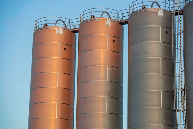 Silos de acero inoxidable en la industria química, silo de plásticos a granel contra un sol naranja