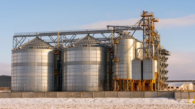 Silos de plata contra el cielo azul en invierno Almacenamiento de granos en invierno a bajas temperaturas Producción para procesamiento secado limpieza y almacenamiento de productos agrícolas harina cereales y granos