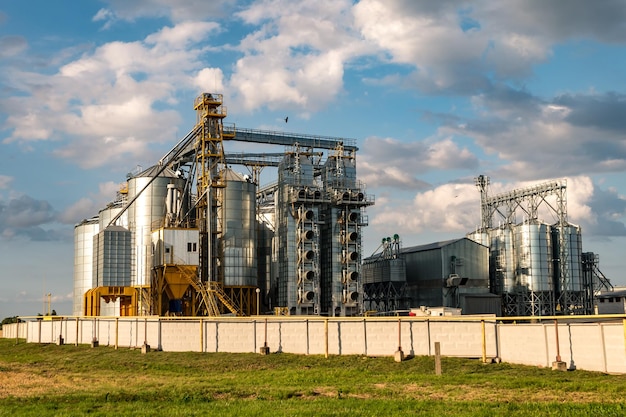 Silos de plata en la planta agroindustrial para el procesamiento, secado, limpieza y almacenamiento de productos agrícolas, harina, cereales y granos con hermosas nubes