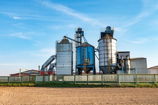 Silos de plata en la planta agroindustrial para el procesamiento, secado, limpieza y almacenamiento de productos agrícolas, harina, cereales y granos con hermosas nubes