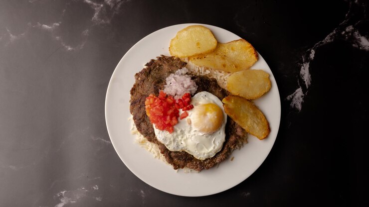 Silpancho Cochabamba comida tradicional boliviana primer plano en el plato sobre fondo oscuro