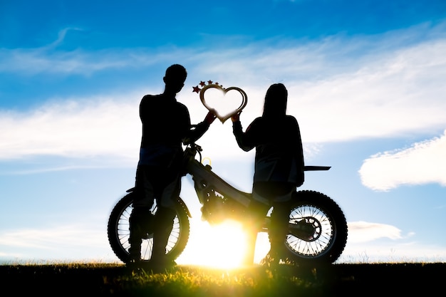 silueta de amantes románticos y motocross con puesta de sol