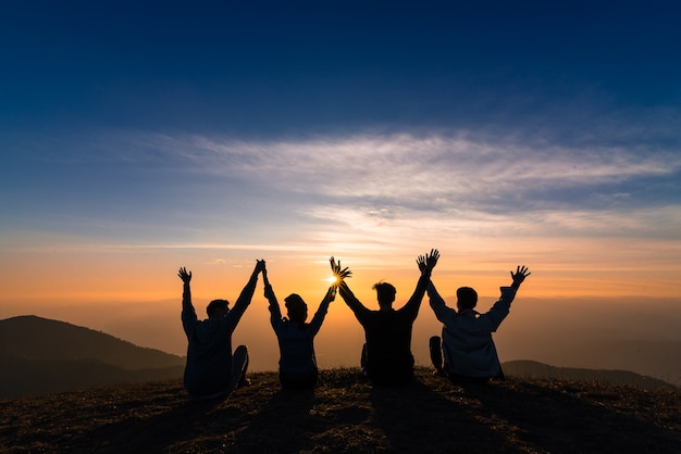 silueta de amigos agitar las manos y sentarse juntos en la felicidad del atardecer