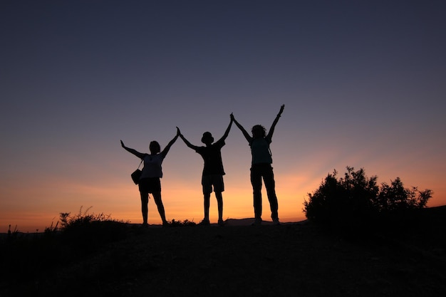 Silueta de amigos con los brazos arriba, fondo de puesta de sol