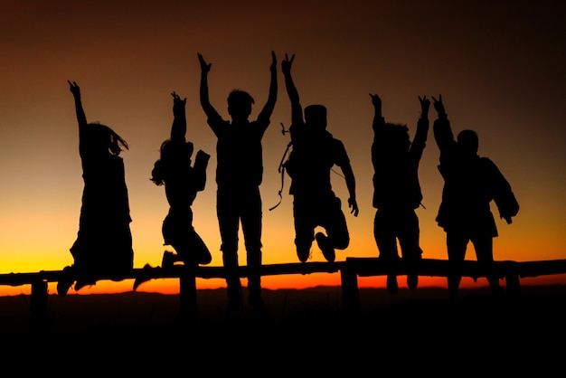 Silueta de amigos felices saltando en el pico de la montaña al amanecer.