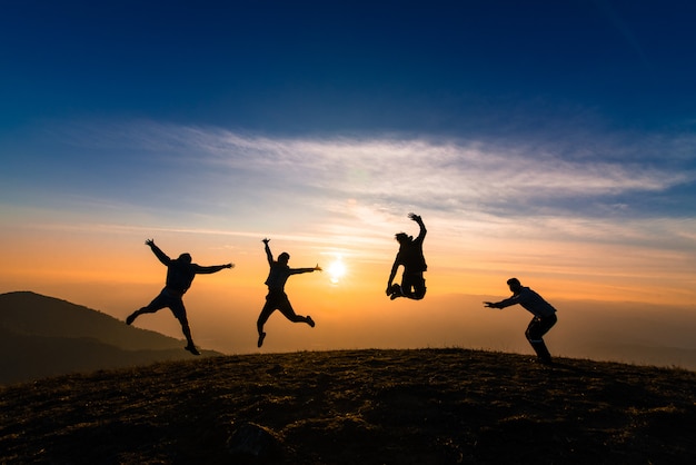 Silueta de amigos saltando al atardecer por felicidad, diversión y concepto de trabajo en equipo