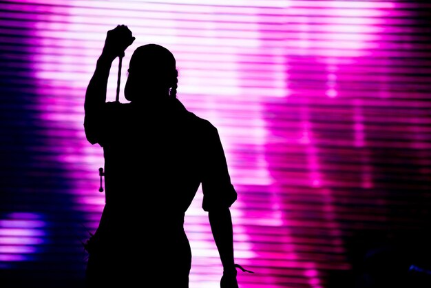 Silueta de un artista cantando en vivo en el escenario frente a un fondo colorido