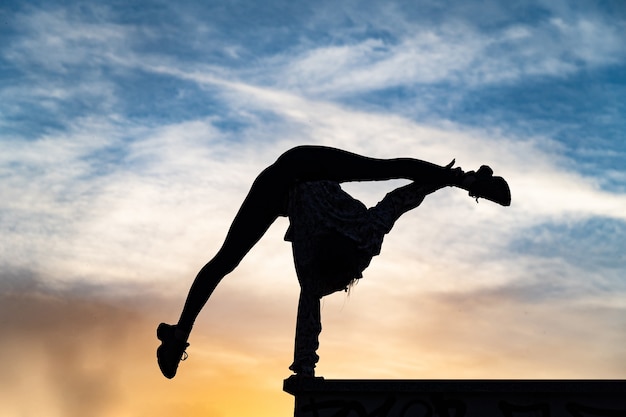 Foto silueta de artista de circo femenino flexible haciendo pino en el concepto de puesta de sol espectacular de indivi ...