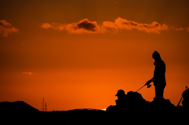 Silueta de caña de pescar de pescador al atardecer naranja