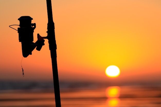 silueta de una caña de pescar en una playa al atardecer