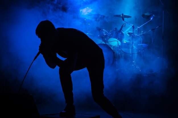 Silueta de un cantante con un micrófono en un concierto en el fondo de la batería en humo con iluminación azul