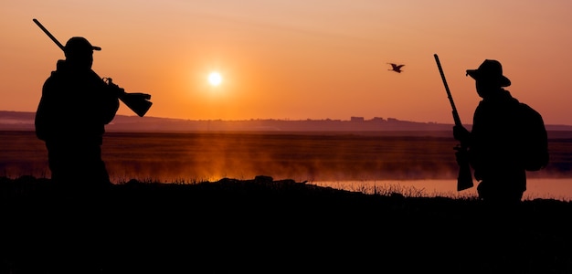 Silueta de un cazador en el fondo del amanecer rojo de la mañana. Está listo con una pistola.