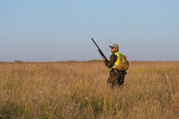 Silueta de un cazador con una pistola en las cañas contra el sol, una emboscada para patos con perros