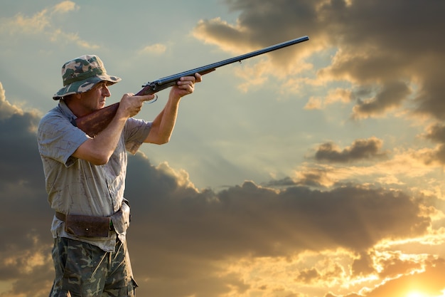 Silueta de un cazador con una pistola en las cañas contra el sol, una emboscada para patos con perros