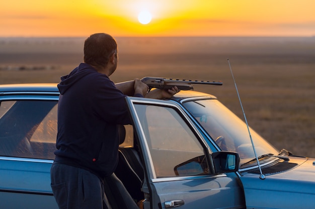 Silueta de un cazador con una pistola en las cañas contra el sol, una emboscada para patos con perros