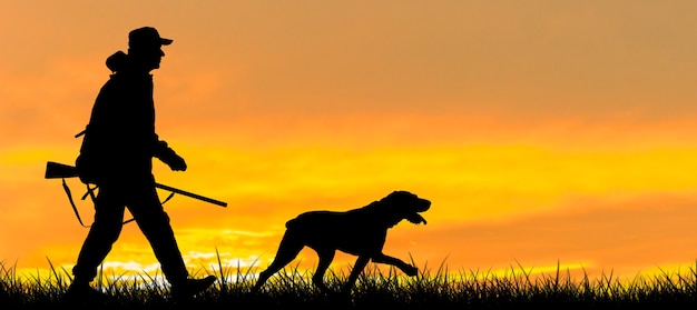 Foto silueta de un cazador con una pistola en las cañas contra el sol una emboscada para patos con perros