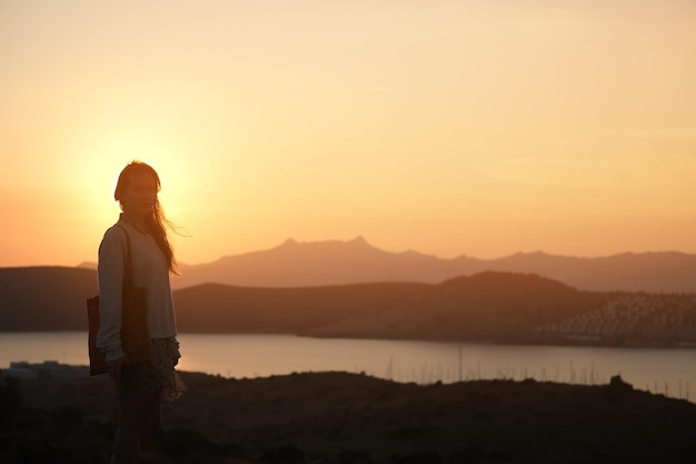 Silueta de una chica al atardecer, persona parada en una colina al fondo del mar al amanecer, amanecer