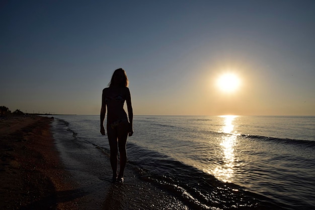 Foto silueta de una chica contra la puesta de sol junto al mar