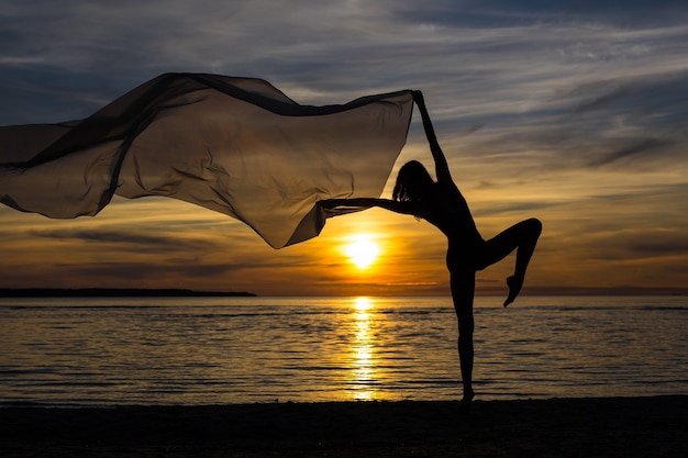 Silueta de chica delgada sexy posando con bufanda en la playa al atardecer