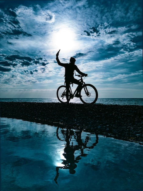 Silueta de un chico en bicicleta de montaña contra el fondo del mar y hermosas texturas de nubes