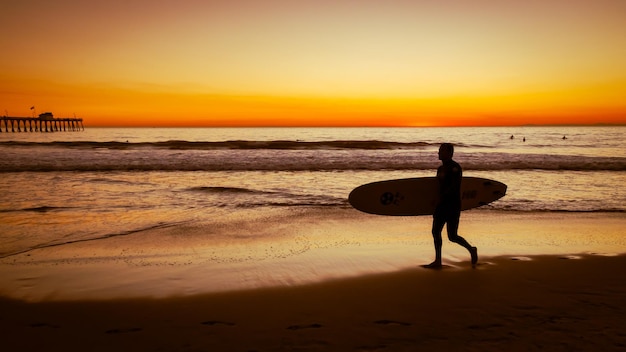 Silueta de un chico caminando con tabla de surf en la playa de San Clemente durante la puesta de sol