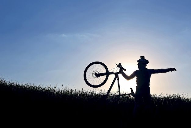 Silueta de un ciclista con una bicicleta en la hierba en el sunxA