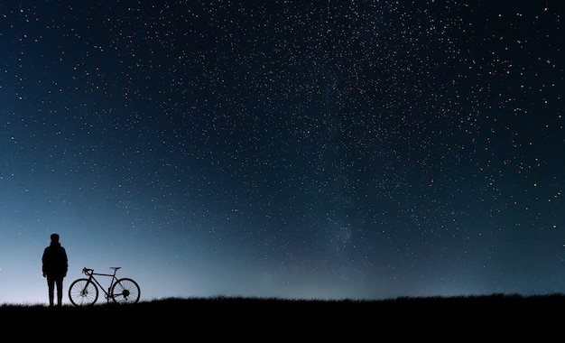 Silueta de un ciclista con una bicicleta de pie cerca del cielo estrellado.