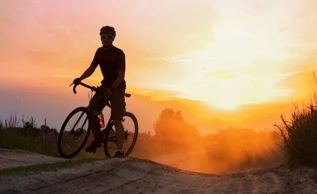 Silueta de ciclista cabalgando sobre un rastro de polvo al fondo del atardecer.