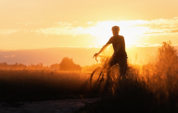 silueta, de, ciclista, en, un, campo, camino de tierra, en, ocaso