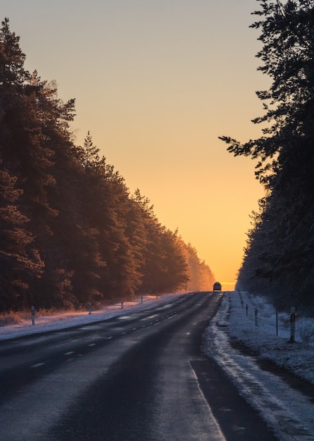 Silueta de un coche en la carretera asfaltada en la luz del atardecer de invierno cubierto de nieve.