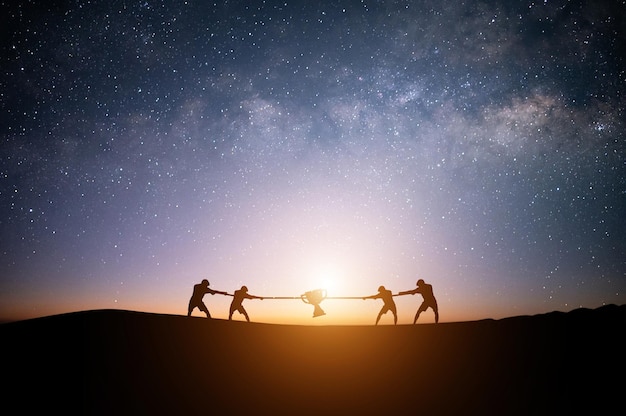 Silueta de cuatro jóvenes empresarios tirando de la guerra con una cuerda en la cima de la montaña con cielo nocturno y fondo de estrellas Concepto de rivalidad de competencia empresarial desafío o disputa