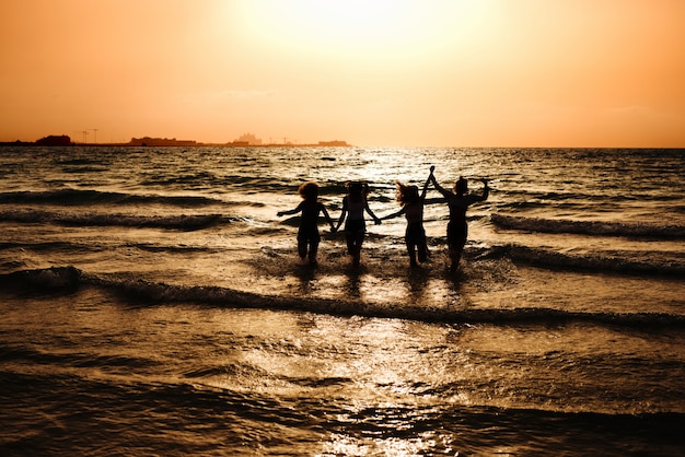 Silueta de cuatro niñas corriendo en el mar y cogidos de la mano.